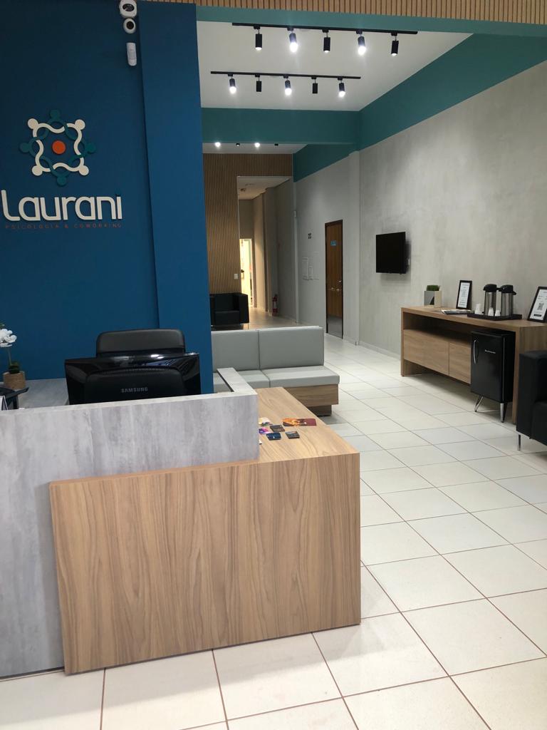 Recepção do Laurani Coworking em Campo Mourão, com balcão de madeira, poltrona e parede azul petróleo com a marca